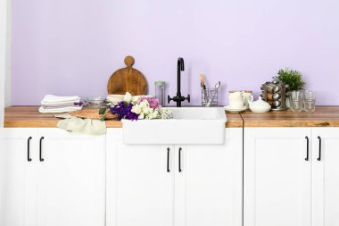 Seramik lavabo güzel çiçekler ve mutfak gereçleri leylak duvarın yanındaki tezgahlarda.