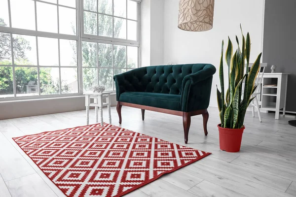 Yeşil kanepeli, çiçekli ve kırmızı halılı aydınlık oturma odasının içi.