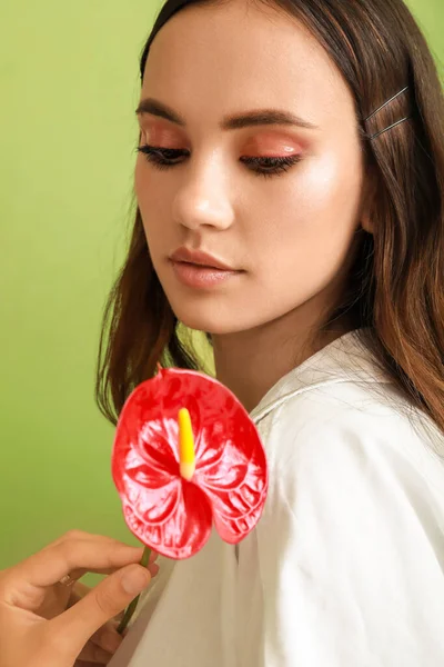 Güzel genç bir kadın yeşil arka planda elinde anthurium çiçeğine bakıyor.