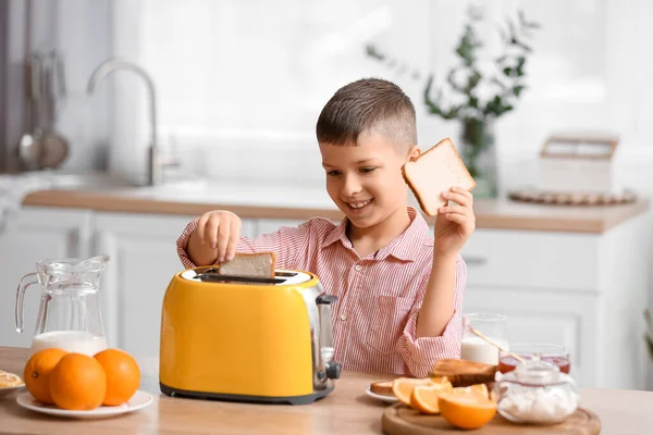 Sevimli küçük çocuk mutfakta ekmek kızartma makinesine ekmek dilimleri koyuyor.