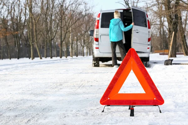 Soğuk kış gününde acil durum levhası ve kırık arabanın yanında bir kadın.
