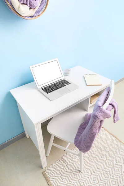 Boş ekranlı dizüstü bilgisayar, mum ve not defteri mavi duvarın yanında.