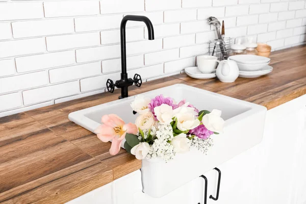 Beyaz tuğla duvarın yanındaki tezgahta güzel çiçeklerle lavabo