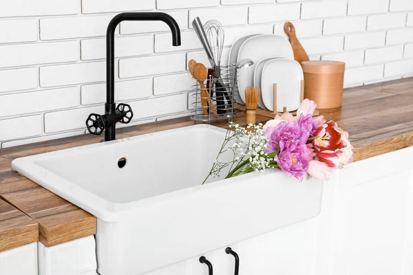 Seramik lavabo, güzel çiçekler ve mutfak gereçleri beyaz tuğla duvarın yanında.