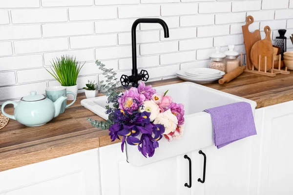 Seramik lavabo, güzel çiçekler ve mutfak gereçleri beyaz tuğla duvarın yanında.