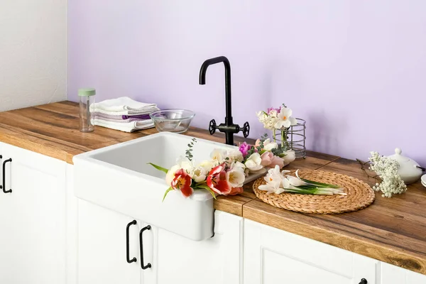 Güzel çiçeklerle lavabo ve mutfak aletleri leylak duvarın yanındaki tezgahlarda.