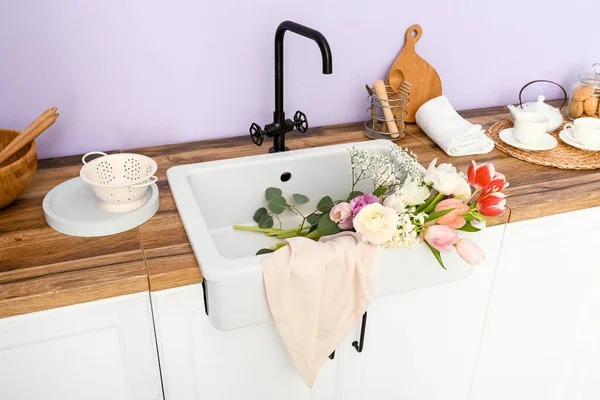 Güzel çiçeklerle lavabo ve mutfak aletleri leylak duvarın yanındaki tezgahlarda.