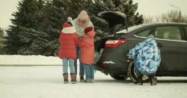 Mutlu aile kış günü arabanın yanında sıcak çay içiyor.