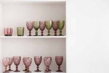 Beyaz duvarın yanında farklı gözlüklü raf ünitesi.