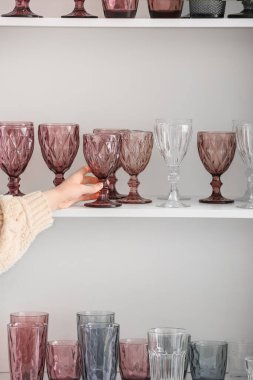Kadın raf ünitesinden şık boş bardaklar alıyor.
