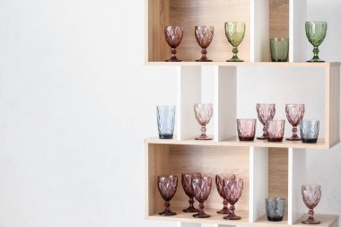 Beyaz duvarın yanındaki ahşap rafta farklı boş bardaklar var.