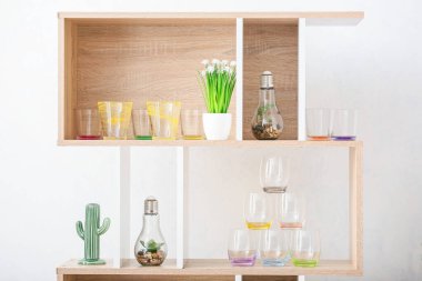 Beyaz duvarın yanındaki ahşap raf ünitesinde modern gözlükler ve şık dekorlar.