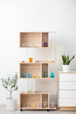 Ahşap raf ünitesinde farklı bardaklar ve beyaz duvarın yanındaki çekmeceler.