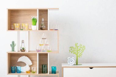 Ahşap raf ünitesinde modern gözlükler ve beyaz duvarın yanındaki çekmecelerde çalar saat.