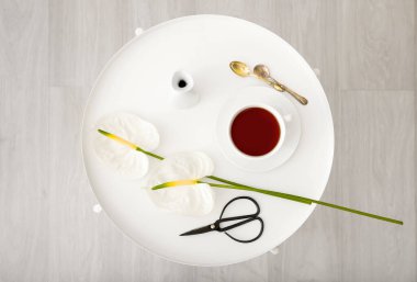 Güzel anthurium çiçekleri, bir fincan çay, vazo ve makas masada.