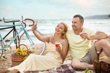 Olgun bir çift yaz günü deniz kenarında şarap içerken selfie çekiyor.