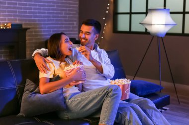Patlamış mısırlı mutlu genç çift akşam evde film izliyor.