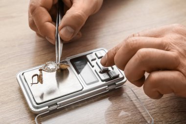 Küpeli bir erkek ve ahşap arka planda mücevher pulları var.