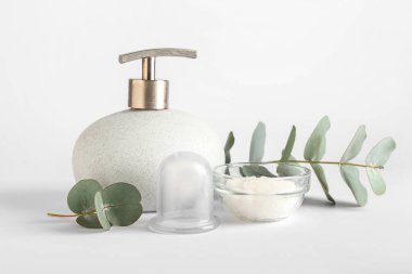 Bottle of cosmetic product, bowl with sea salt, vacuum jar for anti-cellulite massage and eucalyptus branch on white background