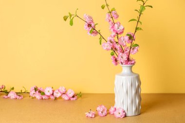 Sarı duvarın yanındaki masada çiçek açan bir vazo.