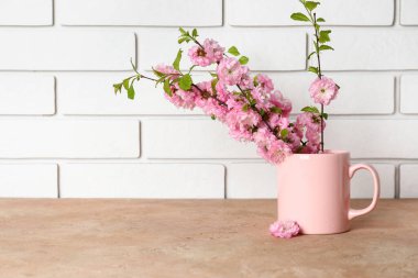 Beyaz tuğla duvarın yanındaki masada çiçek açan dallarla dolu bir kupa.