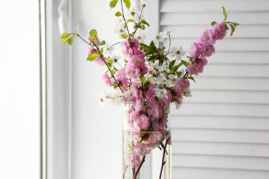 Pencerenin yanında çiçek açan dalları olan vazo, yakın plan