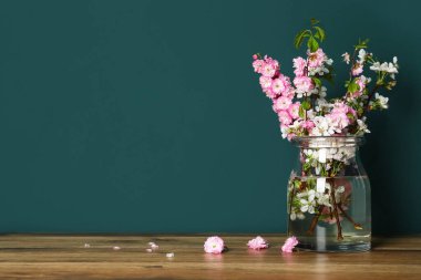 Yeşil duvarın yanındaki ahşap masada güzel dalları olan cam vazo.