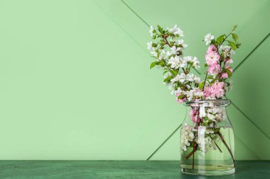 Yeşil duvarın yanındaki masada güzel dalları olan cam vazo.