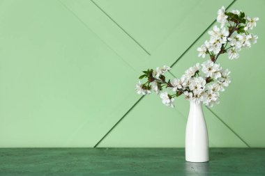Yeşil duvarın yanındaki masada güzel dalları olan beyaz vazo.