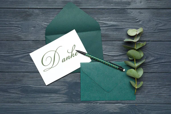 単語Danke ドイツ語のおかげで 封筒やユーカリの枝暗い木製の背景にカード — ストック写真