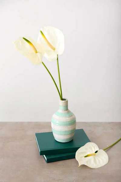 Vase with beautiful anthurium flowers and books on table