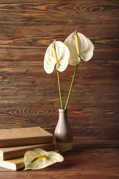 Vase with beautiful anthurium flowers and books on wooden background
