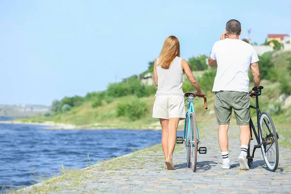 Yaz günü nehir kıyısında bisiklet süren olgun bir çift.