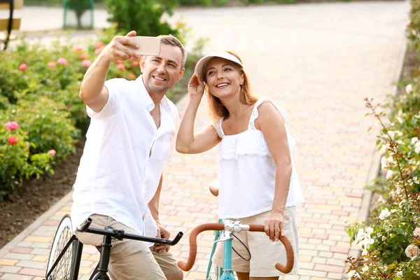 Bisikletli olgun bir çift yaz günü şehir parkında selfie çekiyor.