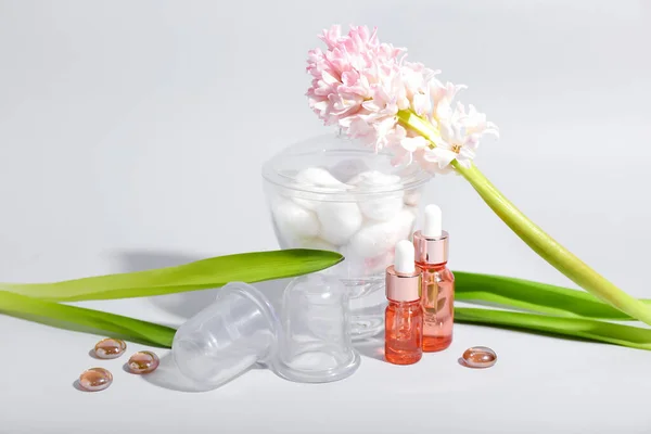 Vacuum jars for anti-cellulite massage, bottles of essential oil, cotton balls and hyacinth flower on white background