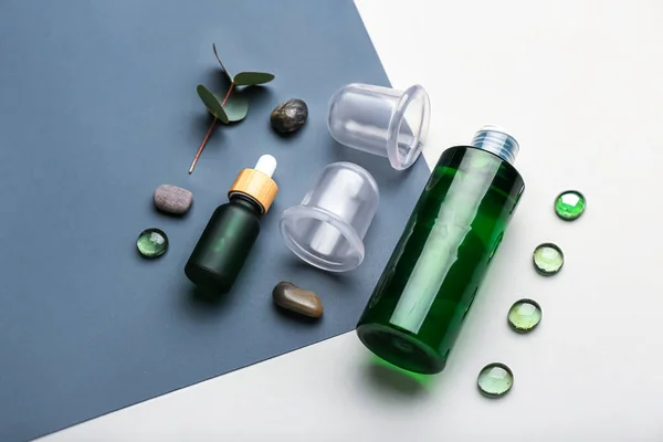 Composition with bottles of cosmetic products, vacuum jars for anti-cellulite massage and glass stones on color background