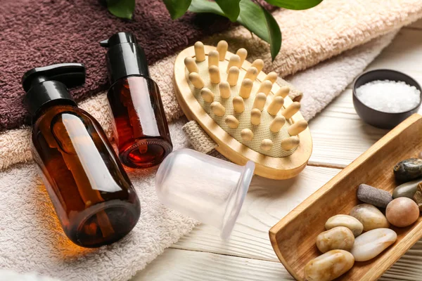Bottles of cosmetic products, vacuum jar for anti-cellulite massage, brush and towels on light wooden background, closeup