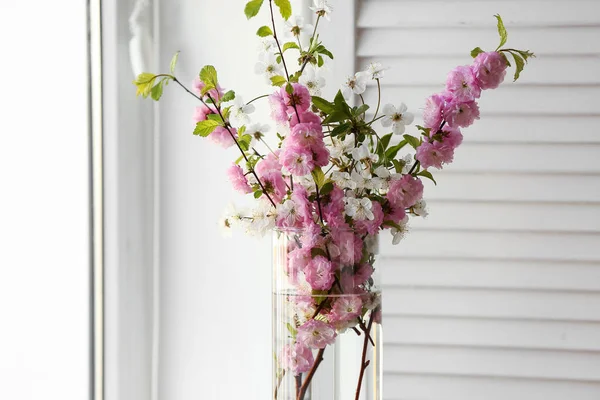 Pencerenin yanında çiçek açan dalları olan vazo, yakın plan