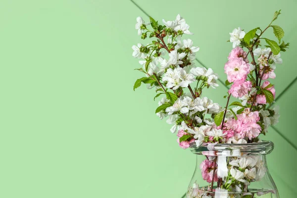 Yeşil duvarın yanında çiçek açan güzel dalları olan cam vazo, yakın plan.