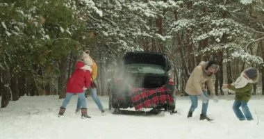 Mutlu aile kış ormanlarında arabanın yanında kartopu oynuyor.