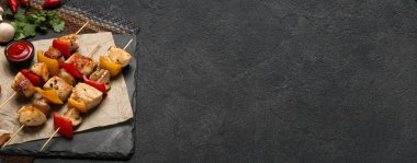 Izgara tavuk şişleri ve siyah arkaplanlı soslu sebzeli pano.