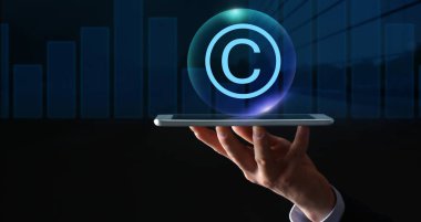 Elinde tablet bilgisayar ve telif hakkı sembolü olan iş adamının eli koyu arkaplanda