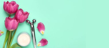 Laleler, krema kavanozu ve turkuaz arka planda yüz masajı aleti. Mesaj için yer var. Anneler Günü kutlaması