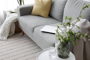 Çiçek açan ağaç dalları ve oturma odasındaki kanepenin yanındaki masada bir bardak su.