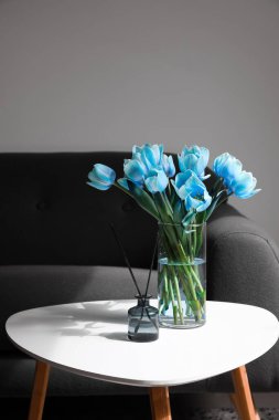 Vase with tulips and reed diffuser on table in living room