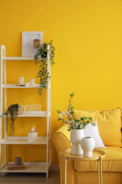 Vases with blooming tree branches on table in stylish living room interior