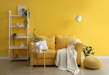 Interior of living room with comfortable sofa, shelf unit and floral decor