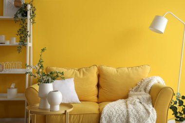 Oturma odasındaki rahat kanepenin yanındaki masada çiçek açan ağaç dalları olan vazolar.