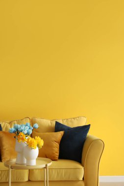 Masada Ukrayna bayrağı renginde vazolar ve sarı duvarın yanında rahat bir kanepe.