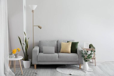 Interior of living room with sofa and floral decor near light wall